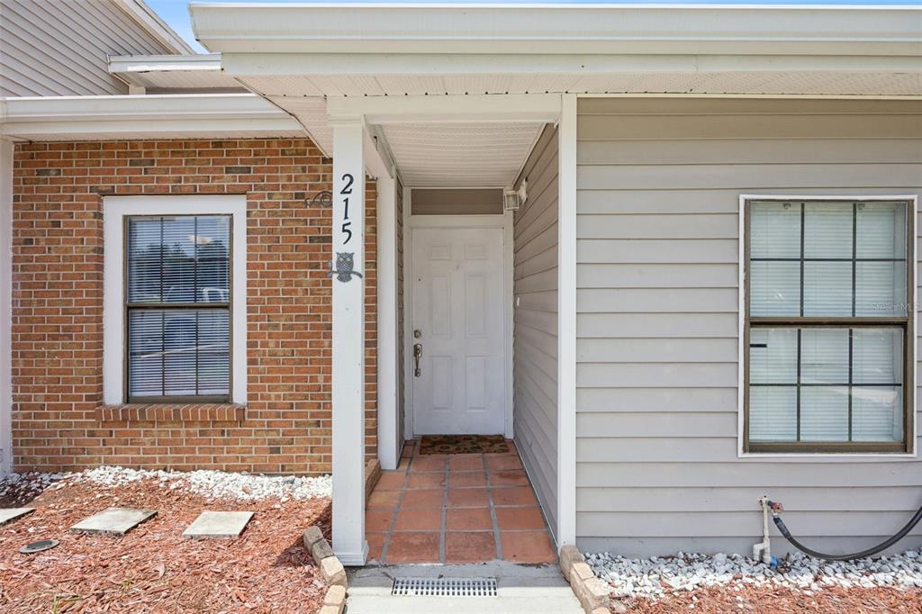 The exterior of a home features a brick facade, gray siding, and a covered entryway — 215 ARBOR CIRCLE, SANFORD, FL