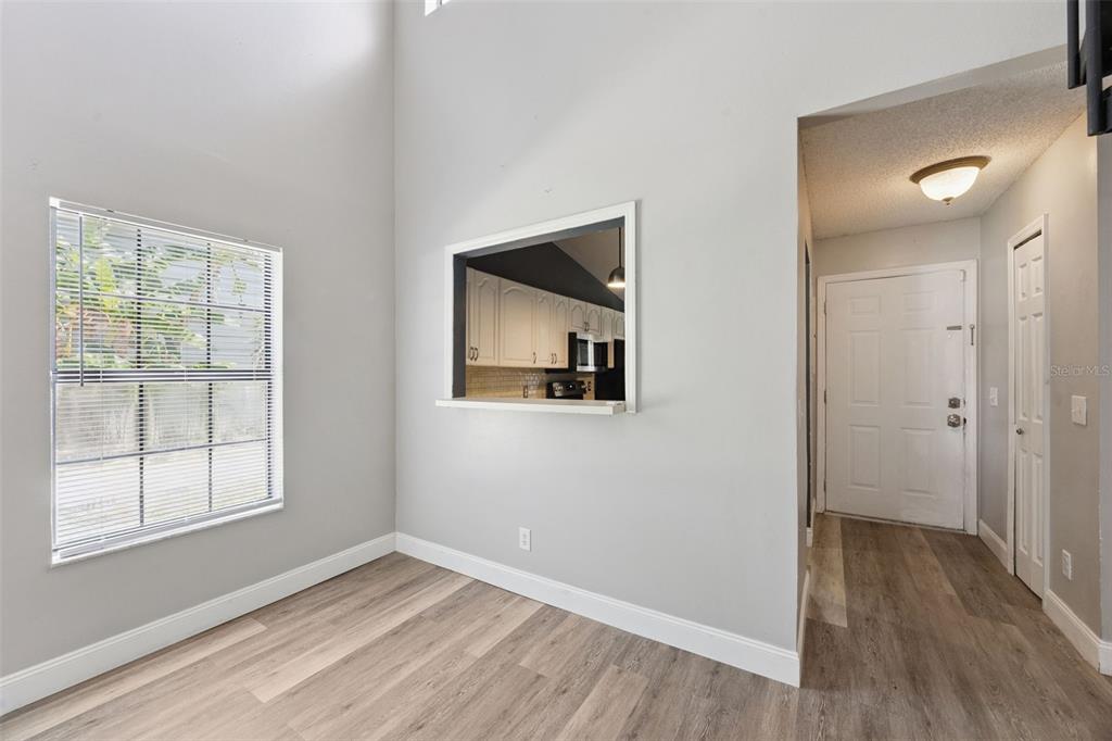 A room with light gray walls, wood-look flooring, a window, and a kitchen pass-through window — 215 ARBOR CIRCLE, SANFORD, FL