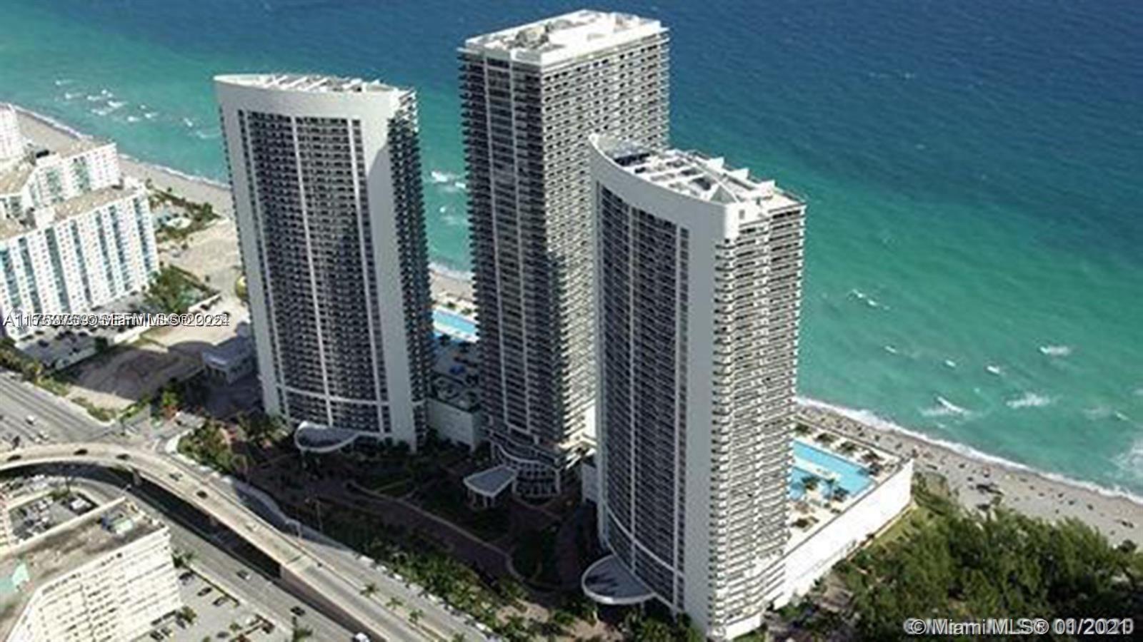 An aerial view shows three tall residential towers situated along a sandy beach — 1830 S Ocean Dr # 3208, Hallandale Beach FL 33009, HALLANDALE BEACH, FL