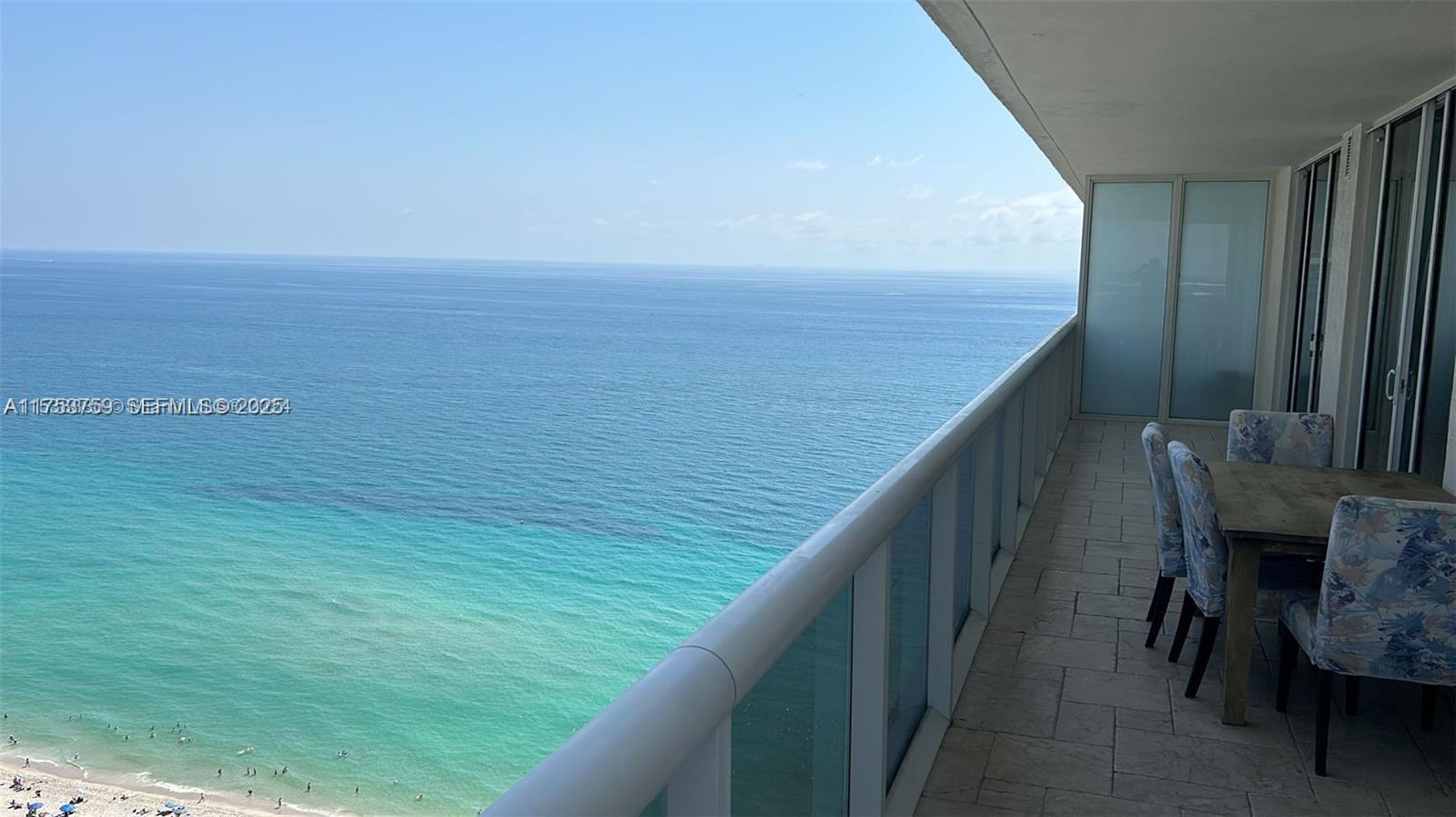 A high-rise balcony features a dining set overlooking the ocean and sandy beach below — 1830 S Ocean Dr # 3208, Hallandale Beach FL 33009, HALLANDALE BEACH, FL