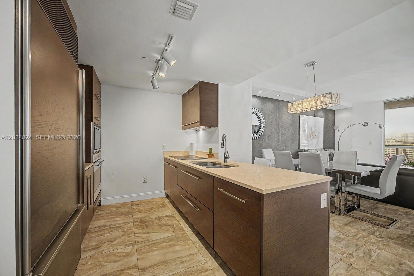 A modern kitchen features dark wood cabinetry, light stone countertops, and tile flooring — 485 Brickell Ave # 2009, Miami FL 33131, MIAMI, FL