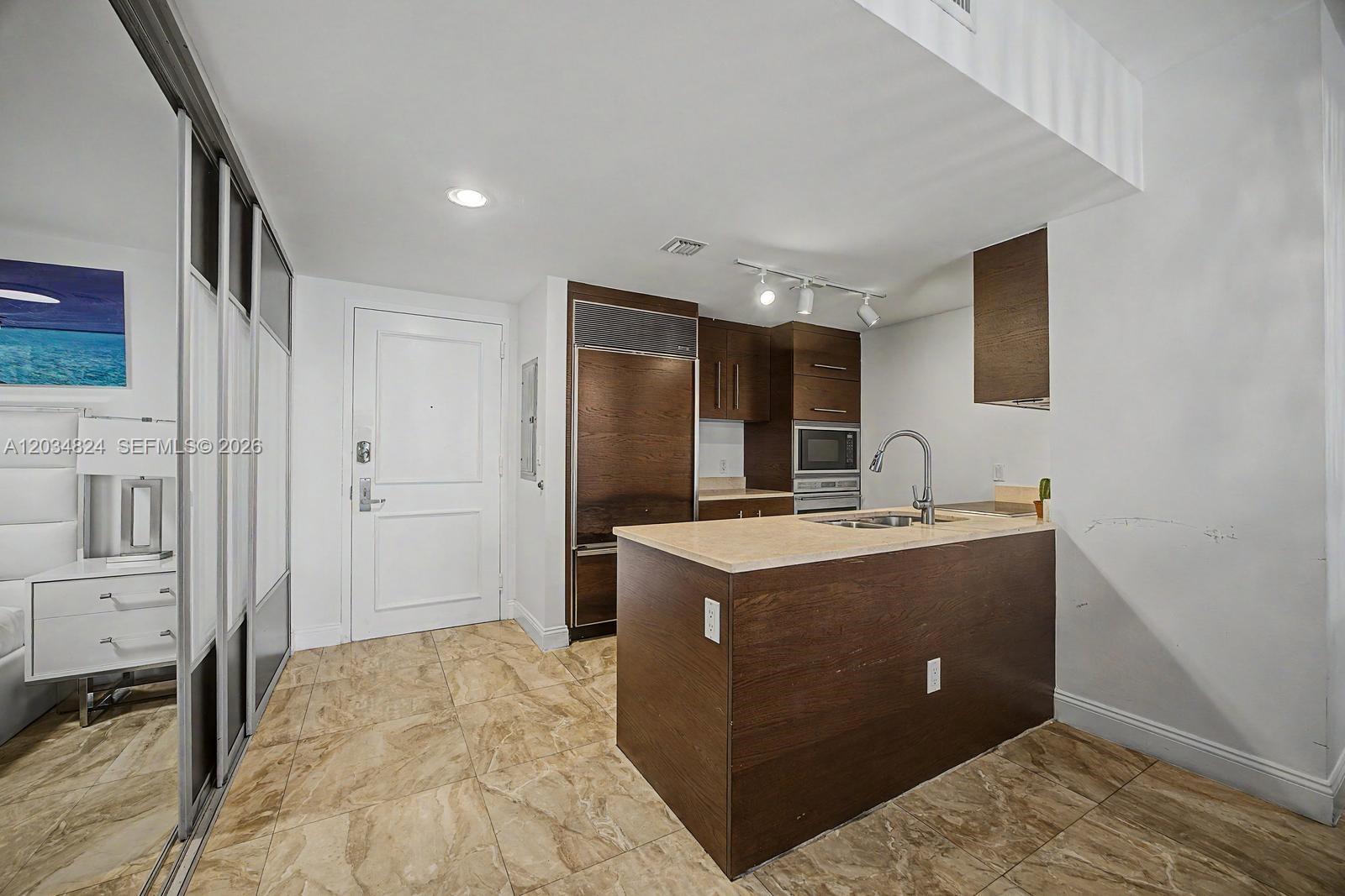 A kitchen features dark wood cabinetry, a stone countertop island, and beige tile flooring — 485 Brickell Ave # 2009, Miami FL 33131, MIAMI, FL