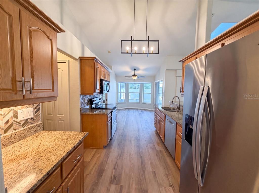 A galley kitchen features wood cabinets, granite countertops, stainless steel appliances, and wood-look flooring — 431 HARBOUR LIGHTS DRIVE, ORMOND BEACH, FL