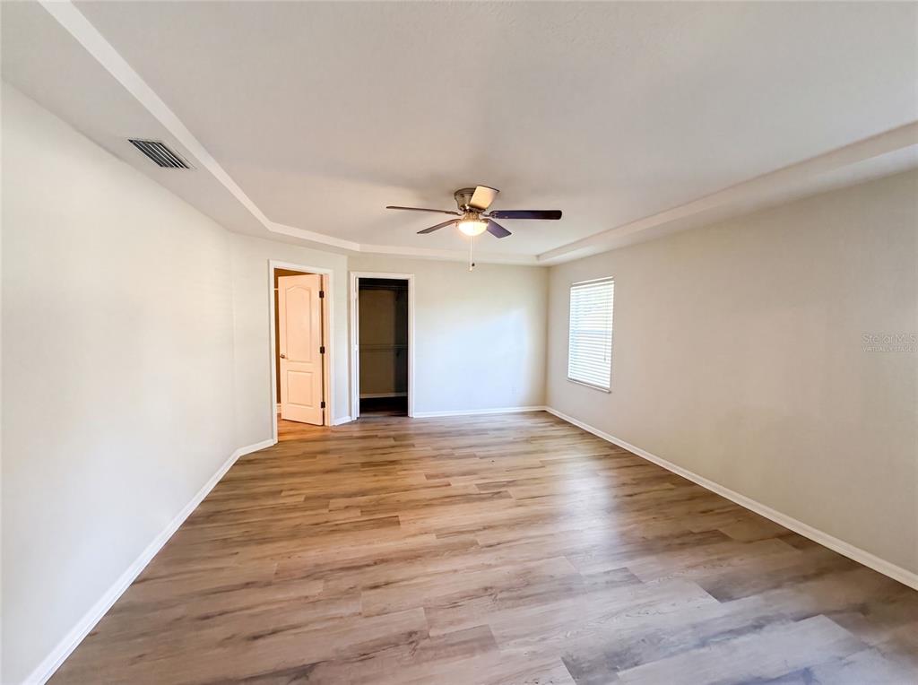 An empty bedroom features light wood-look flooring, a ceiling fan, and a walk-in closet — 431 HARBOUR LIGHTS DRIVE, ORMOND BEACH, FL