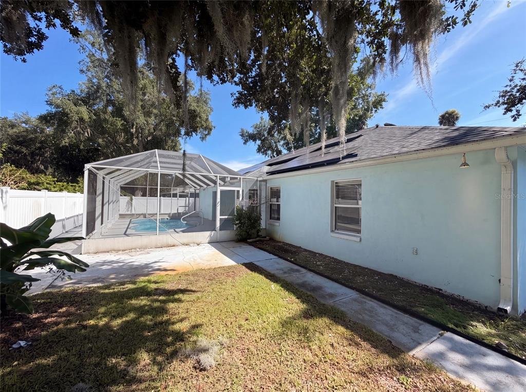 A backyard view of a light blue house with a screened-in pool and solar panels — 431 HARBOUR LIGHTS DRIVE, ORMOND BEACH, FL