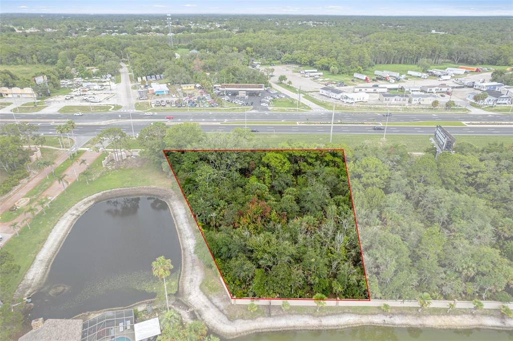 An aerial view shows a wooded, trapezoidal plot of land adjacent to a pond — 00 US HWY 19, HUDSON, FL