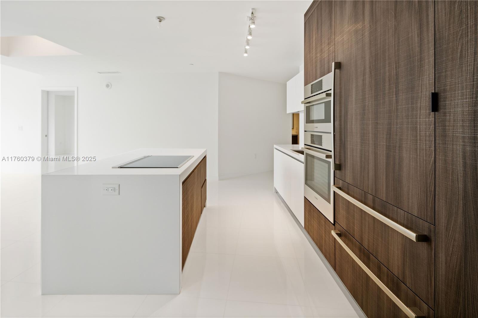 A modern kitchen features a white island with a cooktop and wood-paneled cabinetry with built-in ovens — 851 NE 1st Ave # 4203, Miami FL 33132, MIAMI, FL