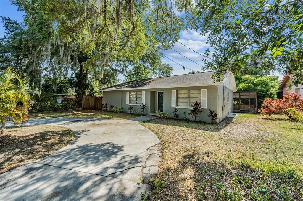 A single-story house with a concrete driveway, white shutters, and large trees in the yard — 9616 N OKLAWAHA AVENUE UNIT 1/2, TAMPA, FL