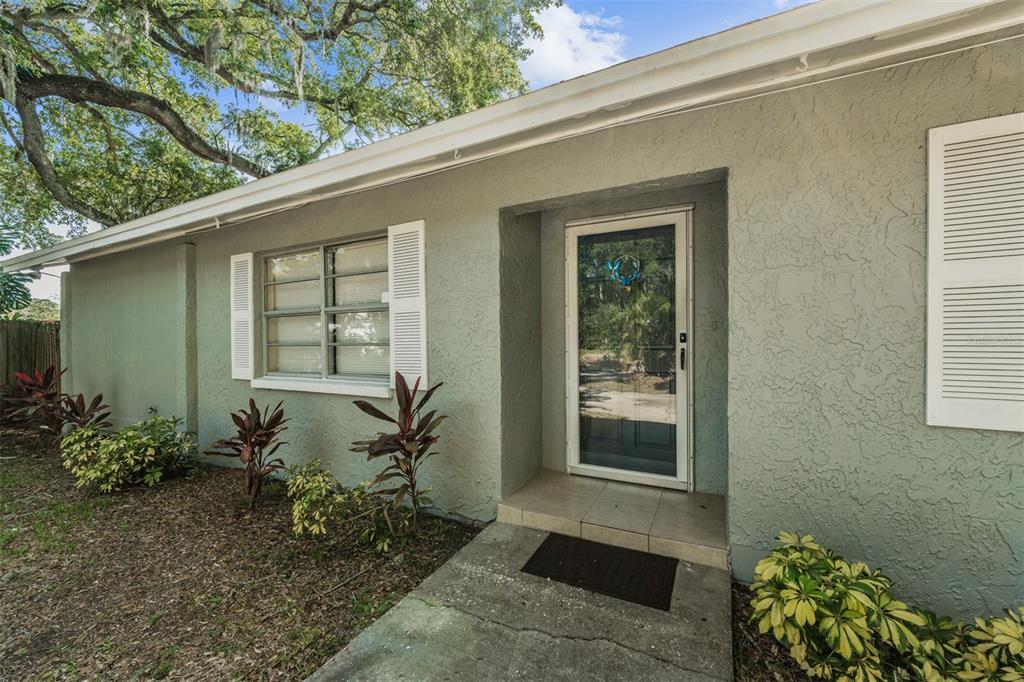 The exterior of a single-story house features a green stucco facade, white shutters, and landscaping — 9616 N OKLAWAHA AVENUE UNIT 1/2, TAMPA, FL