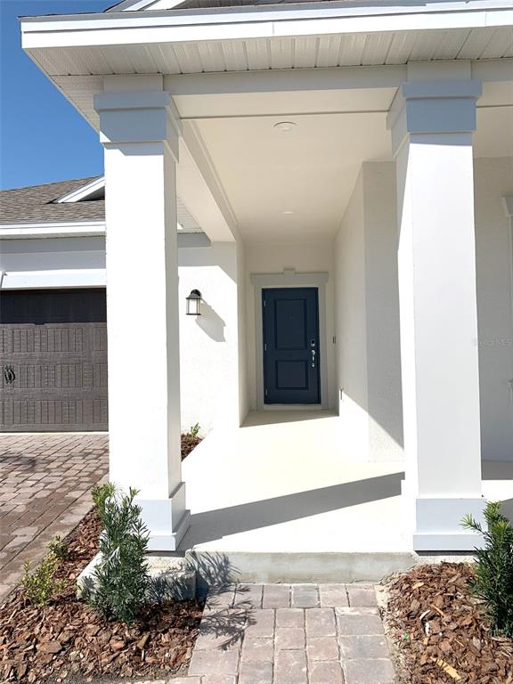 A covered front porch features white columns, a dark blue door, and paver walkways — 1374 BRENTWOOD DRIVE, KISSIMMEE, FL