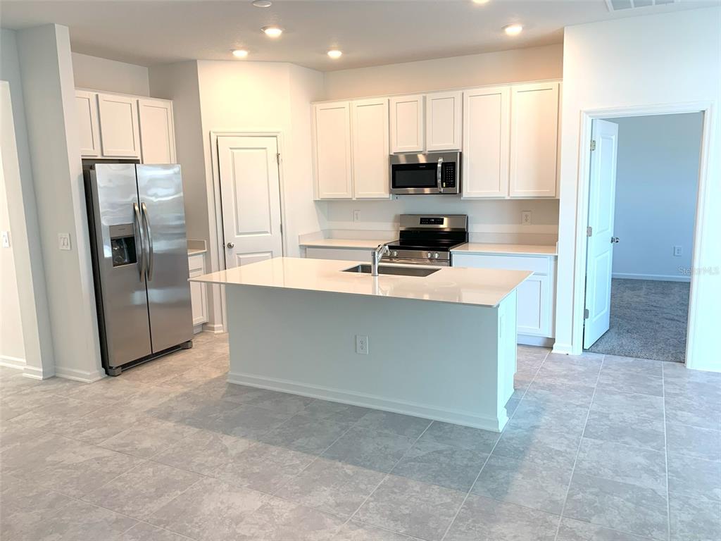 A kitchen features white cabinets, stainless steel appliances, a center island, and gray tile flooring — 1374 BRENTWOOD DRIVE, KISSIMMEE, FL