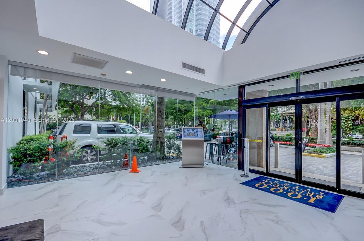 A modern lobby features white marble floors, floor-to-ceiling glass walls, and a vaulted skylight ceiling — 1000 Brickell Ave # 2F, Miami FL 33131, MIAMI, FL