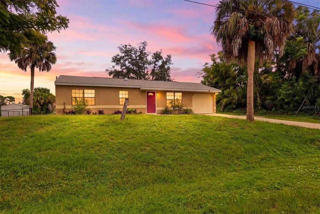 A single-story house with a tan exterior, a red front door, and a grassy yard — 3750 ABA LANE, NORTH PORT, FL