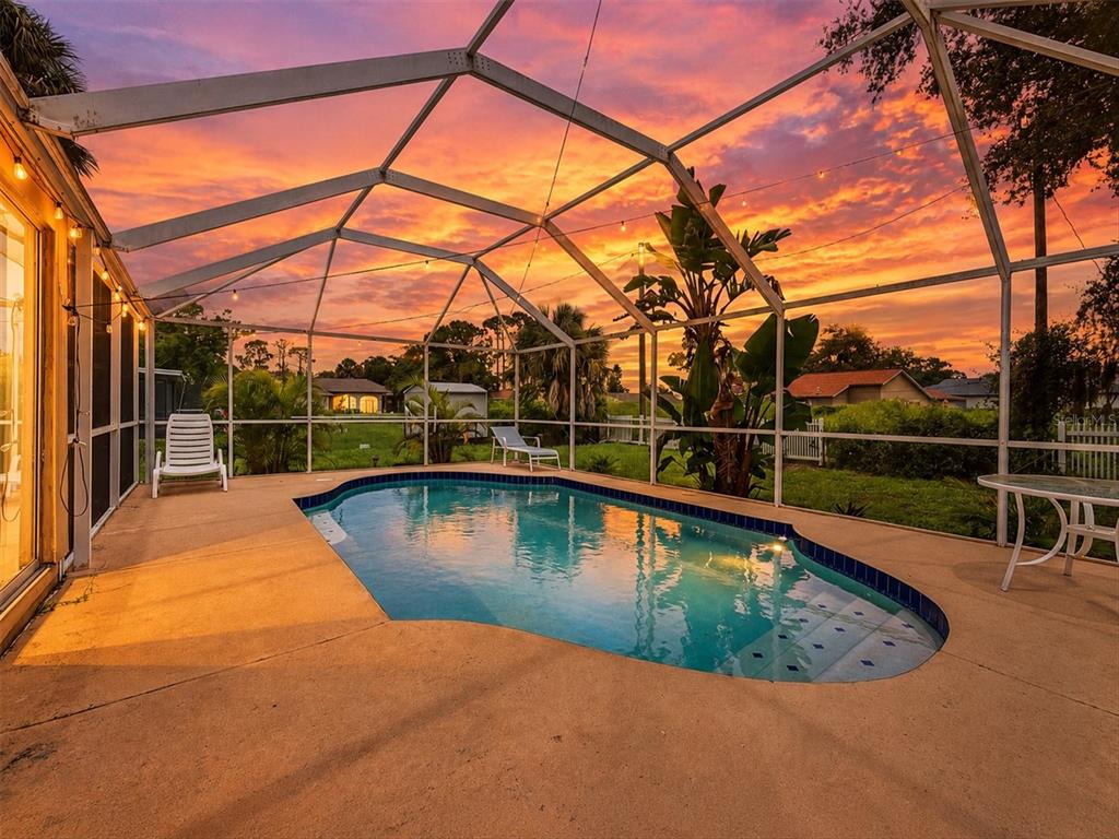 A swimming pool enclosed by a screened lanai at sunset with a view of the backyard — 3750 ABA LANE, NORTH PORT, FL