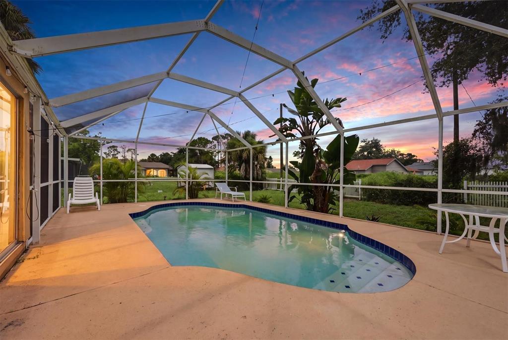 A screened-in pool patio features a kidney-shaped pool, outdoor furniture, and a sunset view — 3750 ABA LANE, NORTH PORT, FL