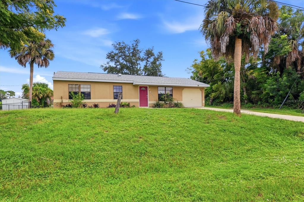 A single-story house with a tan exterior, a red front door, and a grassy yard — 3750 ABA LANE, NORTH PORT, FL