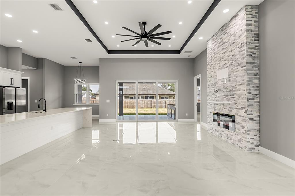 A modern open-concept living room and kitchen featuring a stone fireplace and tile flooring — 28 BUFFALO BILL DRIVE, PALM COAST, FL
