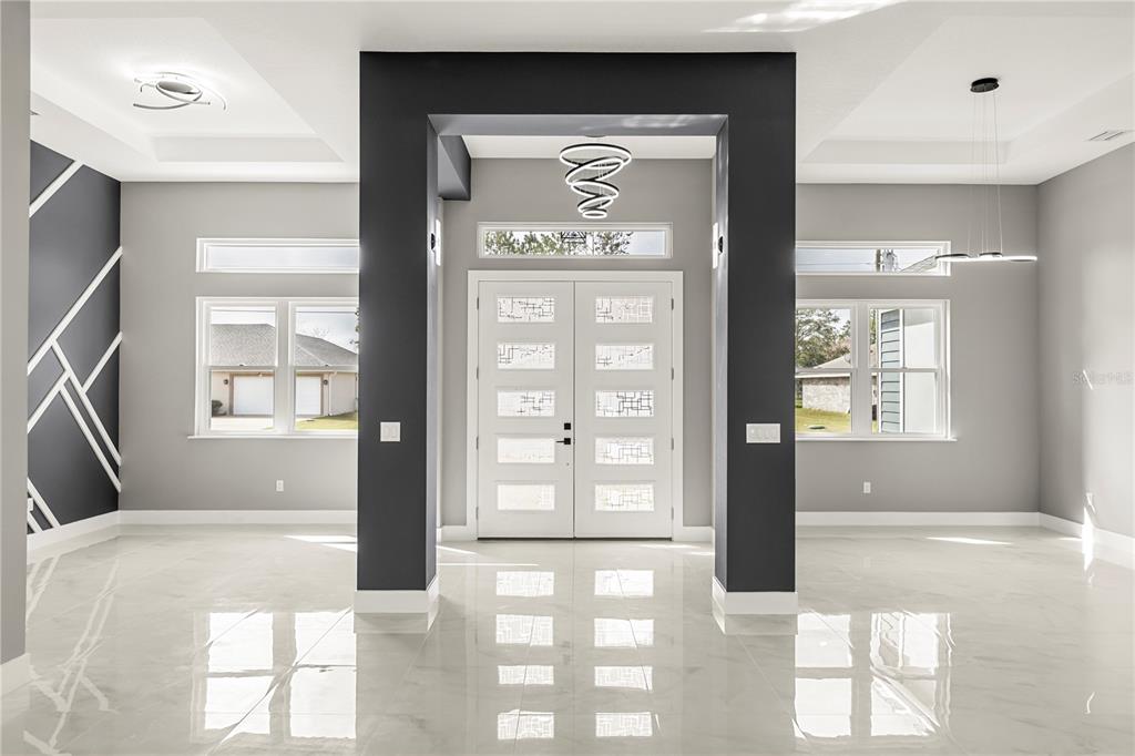 A bright foyer features white double doors, glossy tile floors, and dark accent pillars — 28 BUFFALO BILL DRIVE, PALM COAST, FL