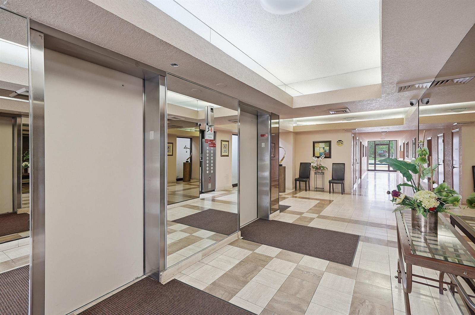 An elevator lobby with tiled floors, mirrored walls, and a glass console table with flowers — 7050 NW 44th Street # 705, Lauderhill FL 33319, LAUDERHILL, FL
