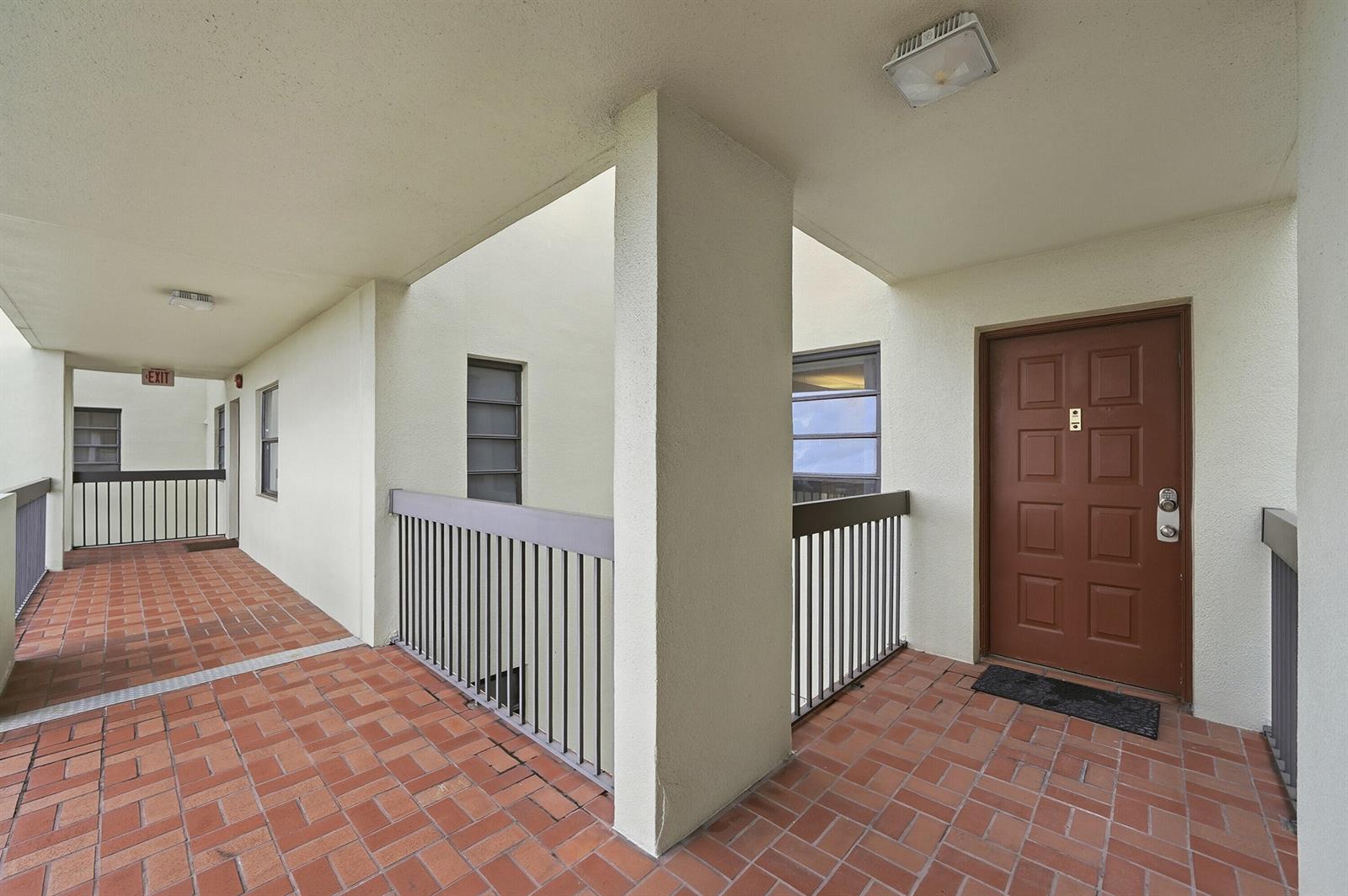 An outdoor apartment hallway with red brick flooring, a brown door, and metal railings — 7050 NW 44th Street # 705, Lauderhill FL 33319, LAUDERHILL, FL