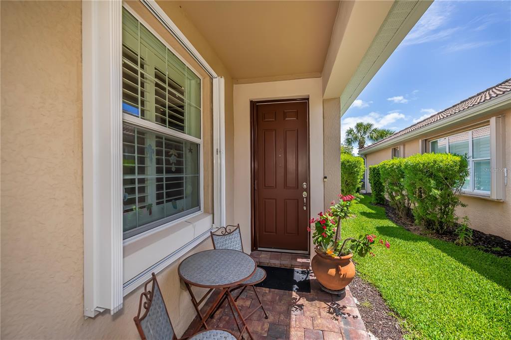 A small patio with a bistro set and potted plant sits outside a brown door — 19060 LAPPACIO STREET, VENICE, FL