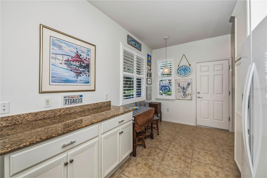 A kitchen features white cabinets, granite countertops, a small dining table, and tiled flooring — 19060 LAPPACIO STREET, VENICE, FL