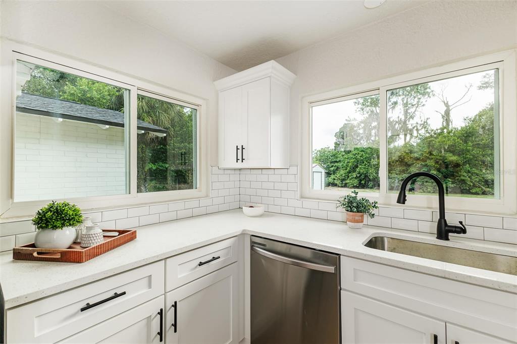 A kitchen corner features white cabinets, a subway tile backsplash, quartz countertops, and two windows — 1470 CAROLINA AVENUE, MULBERRY, FL