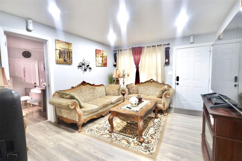 A living room features two ornate sofas, a coffee table, and a rug on wood-look flooring — 414 W ELLA J GILMORE STREET, APOPKA, FL