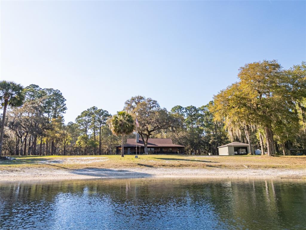A house and detached garage sit on a grassy lot overlooking a lake — 8600 NE 147TH AVENUE ROAD, SILVER SPRINGS, FL