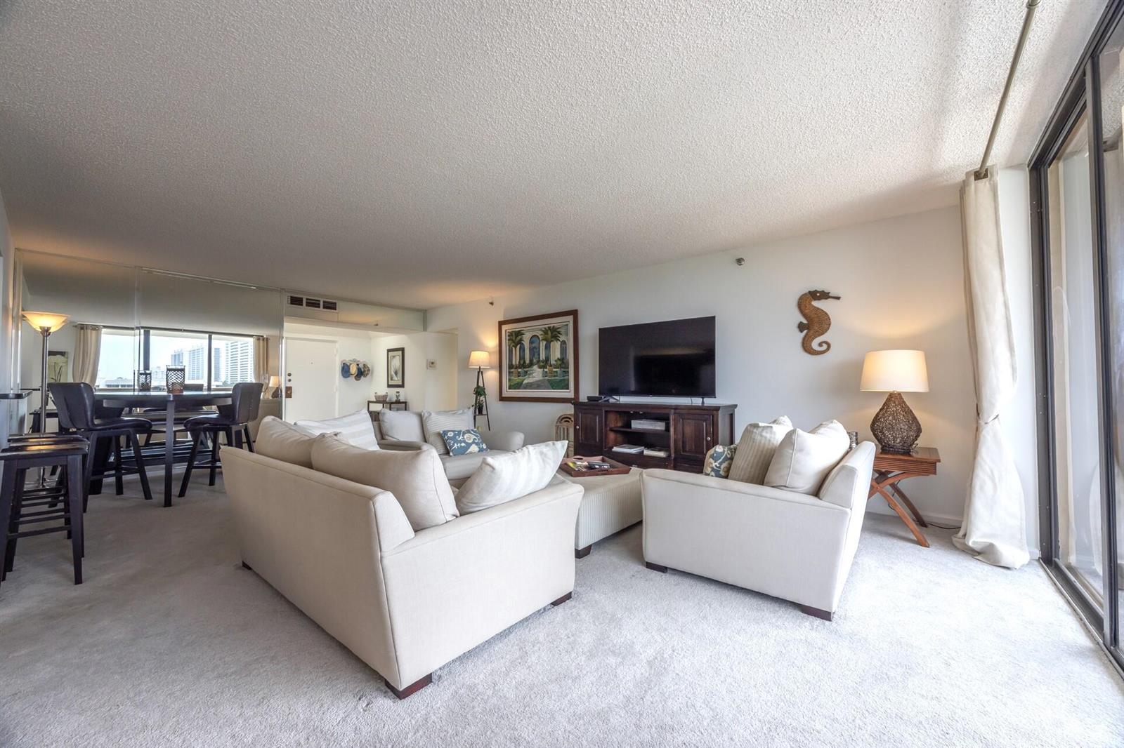 A living room with beige sofas, a television on a wooden stand, and carpeted flooring — 1401 S Ocean Boulevard # 5030, Boca Raton FL 33432, BOCA RATON, FL