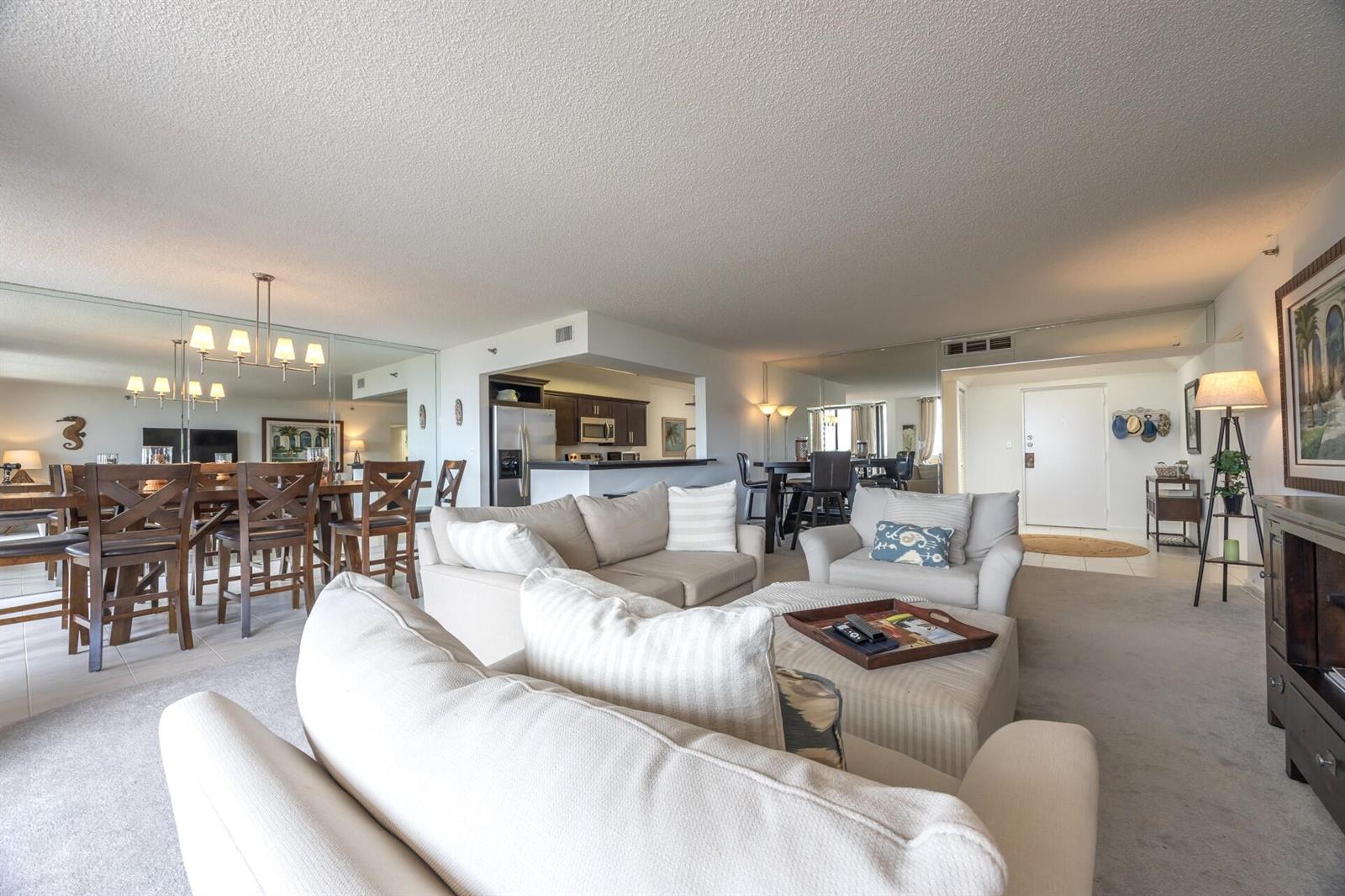 A living room with beige sofas, a central ottoman, and an open-concept kitchen and dining area — 1401 S Ocean Boulevard # 5030, Boca Raton FL 33432, BOCA RATON, FL