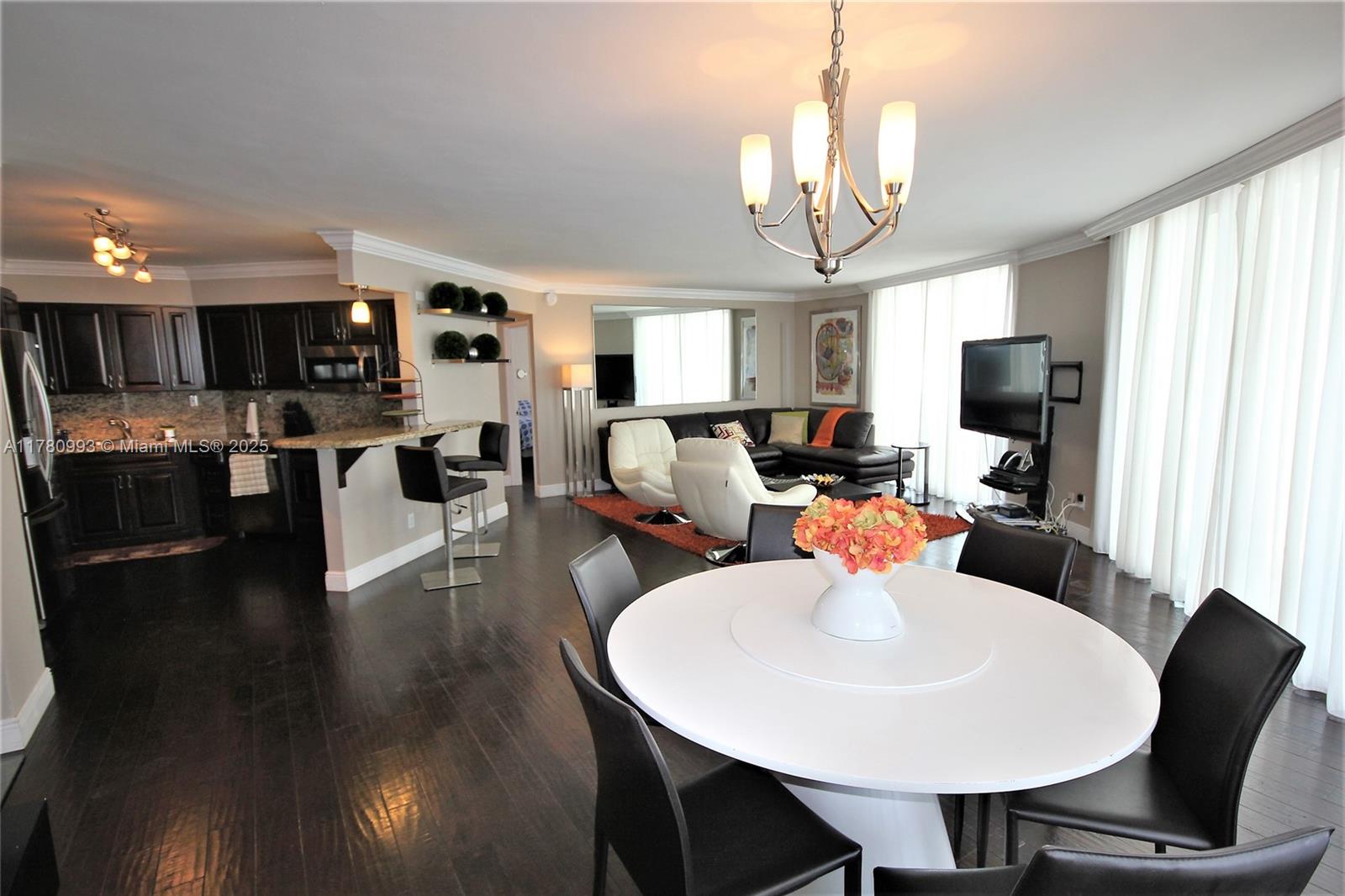 An open-concept living and dining area features dark wood floors, white furniture, and a kitchen — 5151 COLLINS AV # 924, Miami Beach FL 33140, MIAMI BEACH, FL