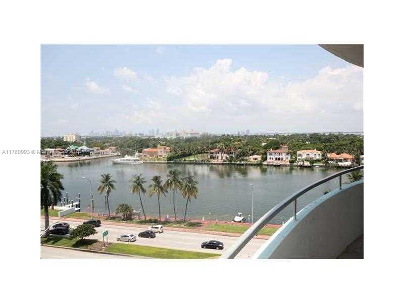 An elevated view of a waterfront road with palm trees, a canal, and distant buildings — 5151 COLLINS AV # 924, Miami Beach FL 33140, MIAMI BEACH, FL