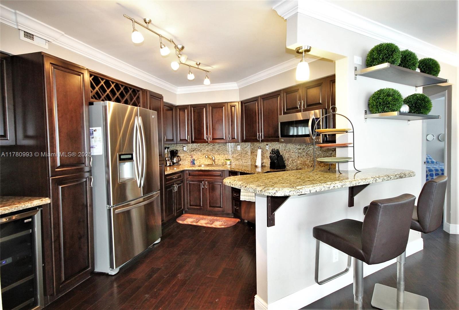 A kitchen features dark wood cabinets, stainless steel appliances, granite countertops, and a breakfast bar — 5151 COLLINS AV # 924, Miami Beach FL 33140, MIAMI BEACH, FL