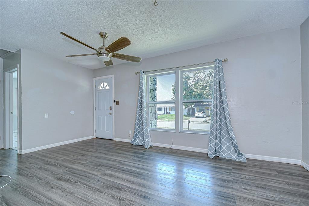 A living room features gray wood-look flooring, a ceiling fan, and a front door — 5325 8TH AVENUE S, GULFPORT, FL