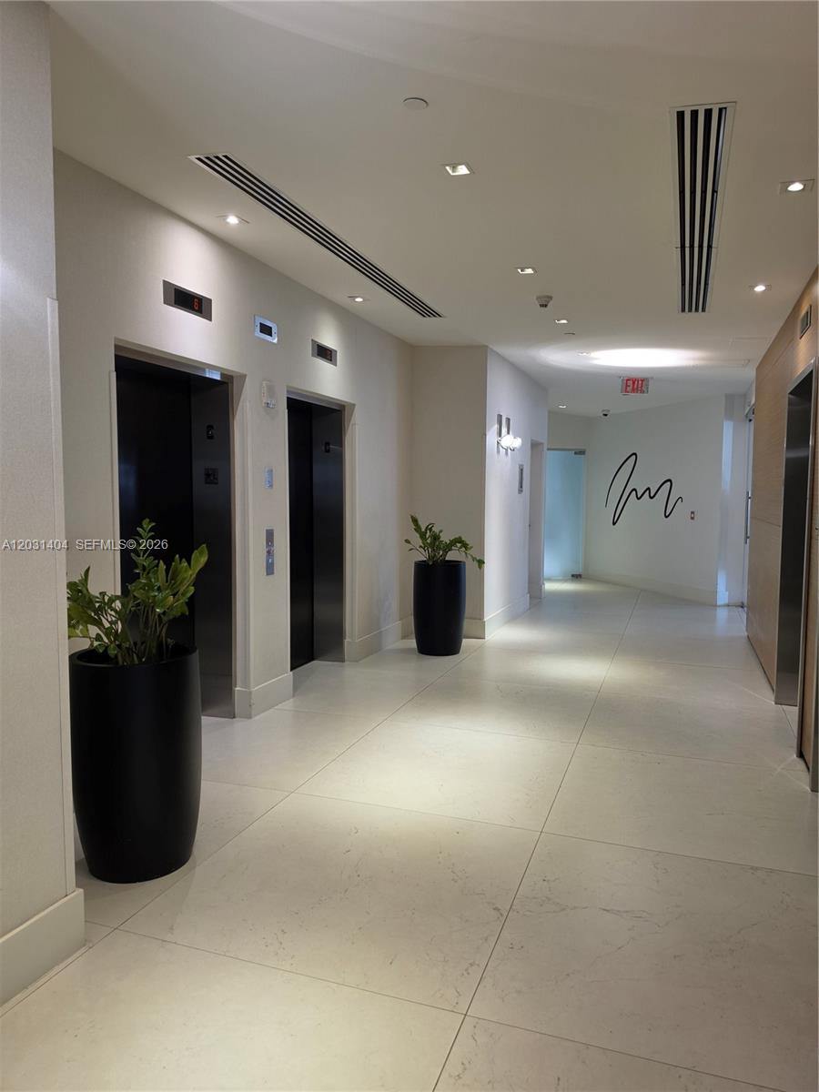 A modern elevator lobby features white tile floors, black planters, and recessed ceiling lighting — 3301 NE 1st Ave # H1206, Miami FL 33137, MIAMI, FL