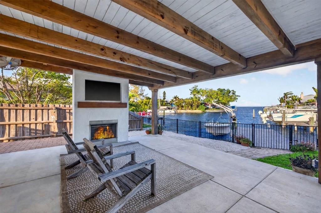 A covered outdoor patio features a fireplace, television, and seating overlooking a waterfront boat dock — 4200 BEACH DRIVE SE, ST PETERSBURG, FL