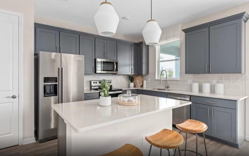 A modern kitchen features gray cabinets, stainless steel appliances, and a central white quartz island — 7456 SUMMER COURT, SARASOTA, FL
