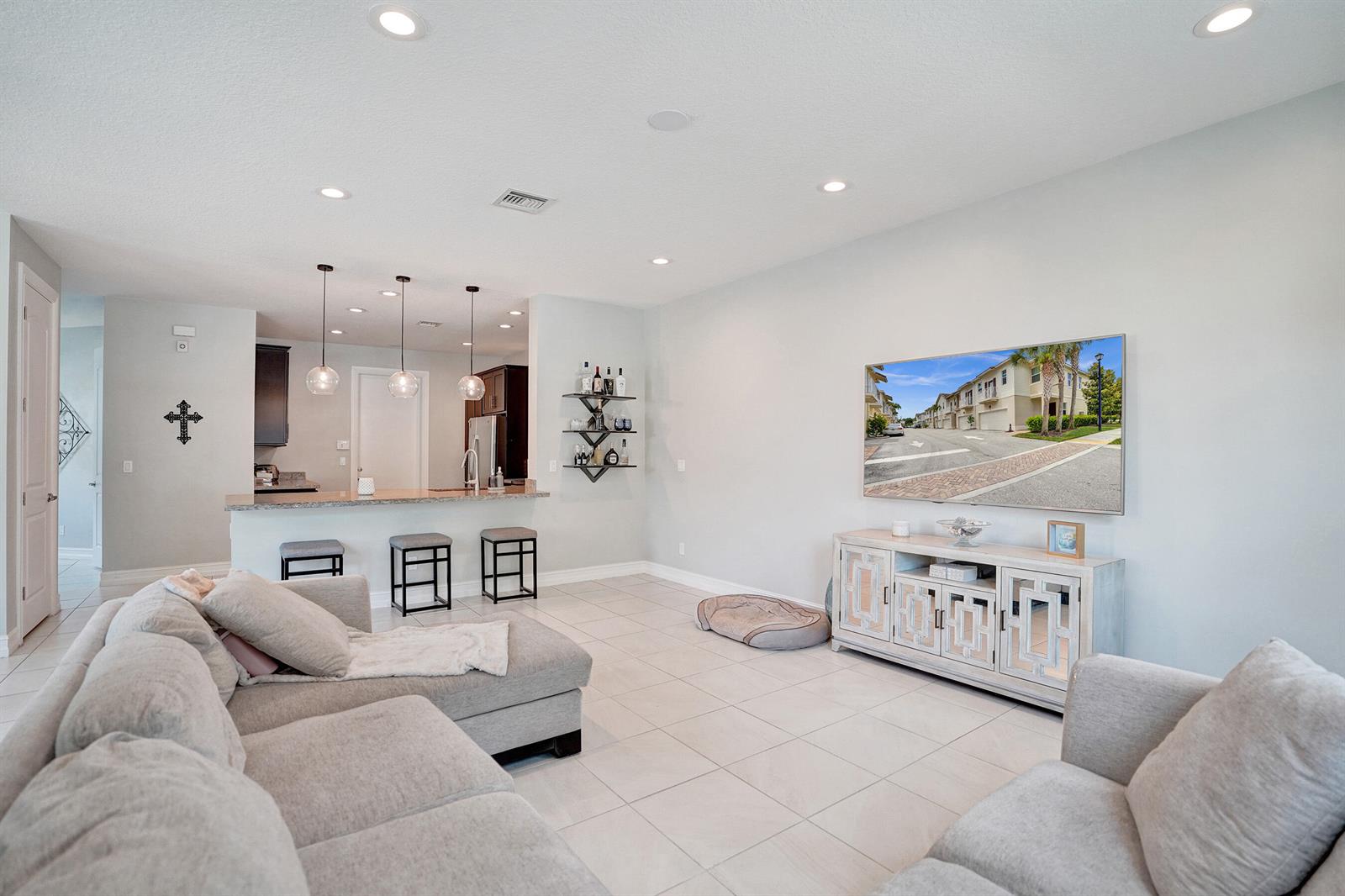 A living room with light tile floors, a sectional sofa, and a wall-mounted television — 99 Palm Lane, Royal Palm Beach FL 33411, ROYAL PALM BEACH, FL