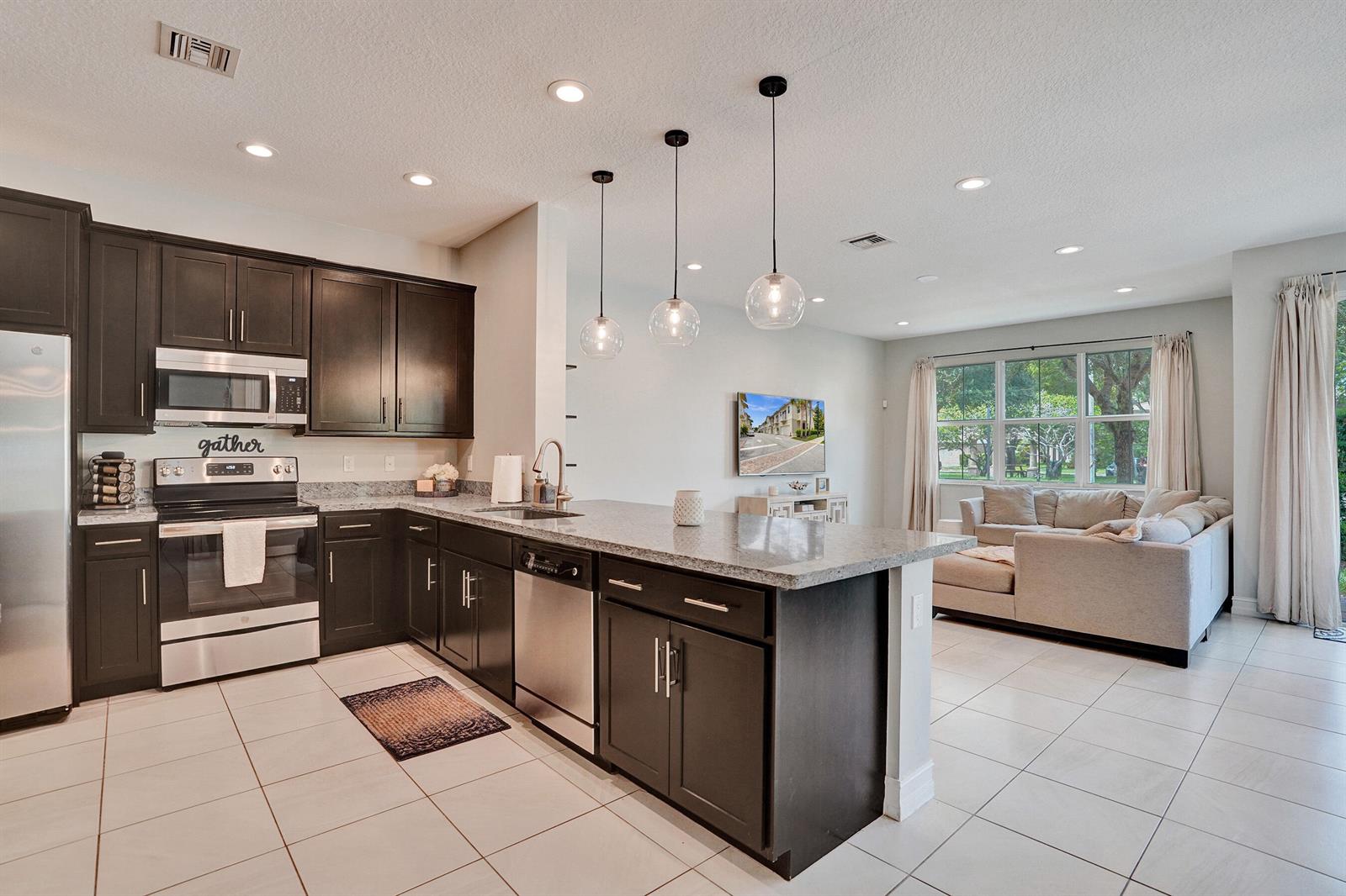 A kitchen with dark cabinets and granite countertops opens into a living room with tile — 99 Palm Lane, Royal Palm Beach FL 33411, ROYAL PALM BEACH, FL