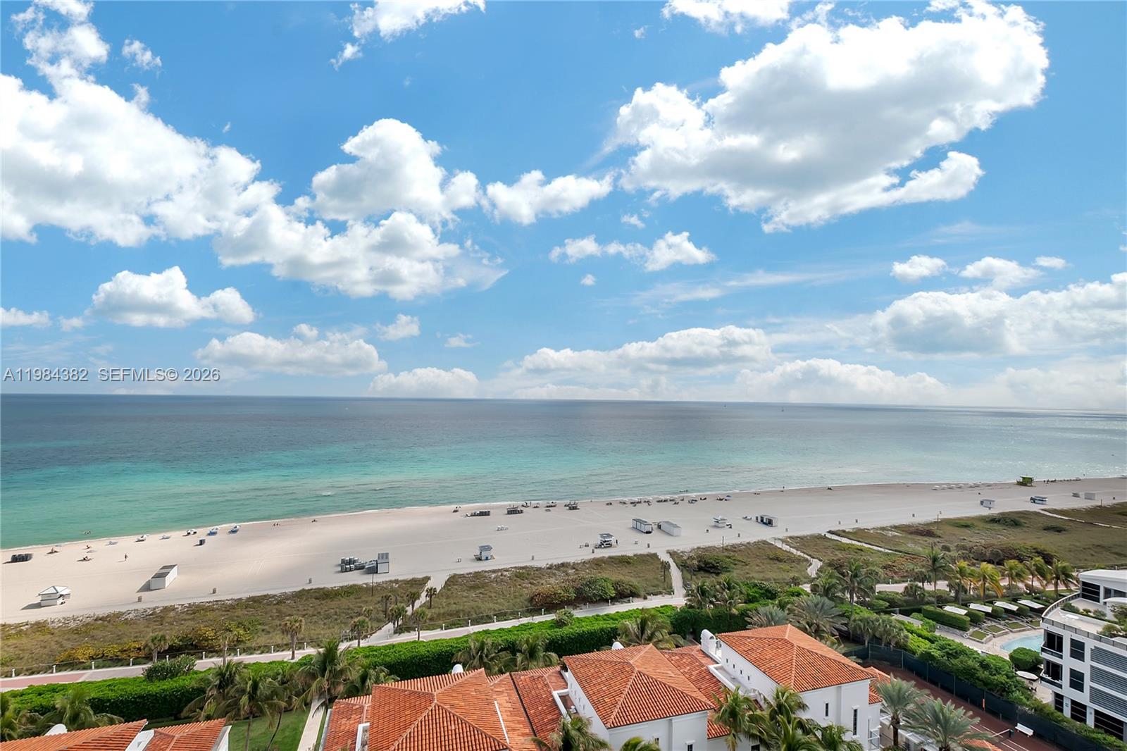 An elevated view of a sandy beach, ocean, and nearby buildings under a cloudy sky — 5959 Collins Ave # 1503, Miami Beach FL 33140, MIAMI BEACH, FL