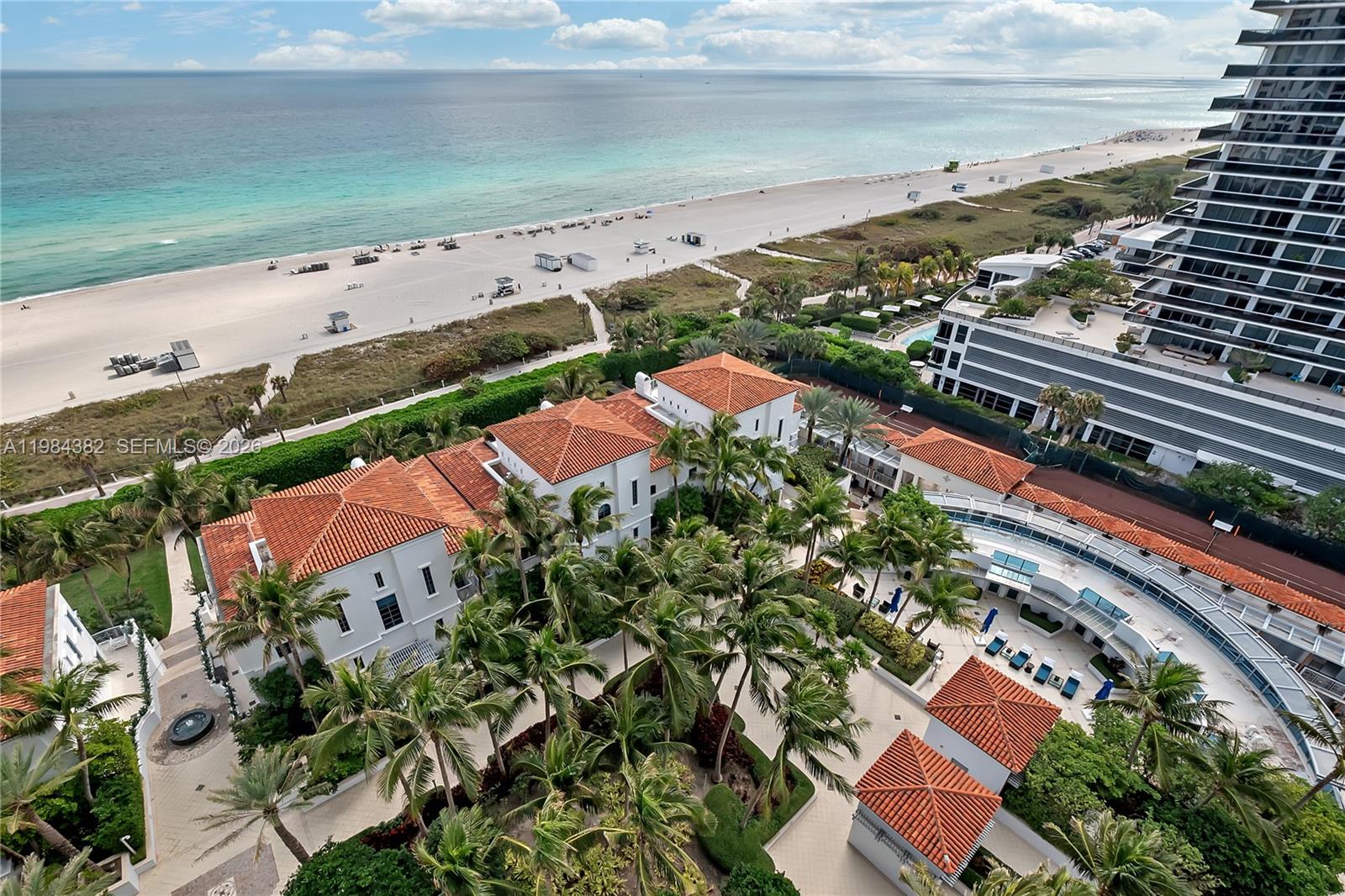 An aerial view shows a beach, a modern high-rise, and a Mediterranean-style complex with palm trees — 5959 Collins Ave # 1503, Miami Beach FL 33140, MIAMI BEACH, FL