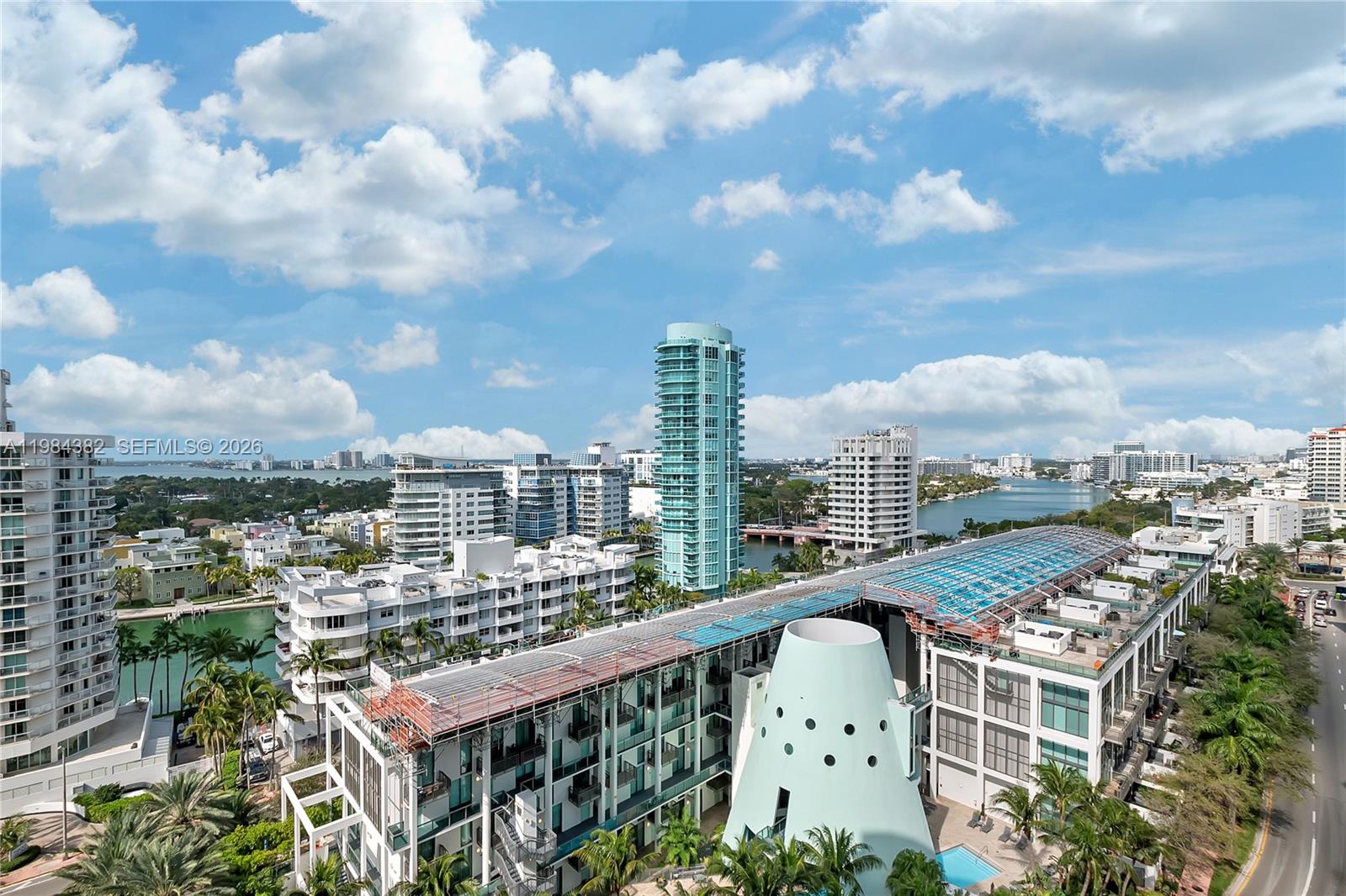 An aerial view shows a modern building with a distinctive conical structure and surrounding city skyline — 5959 Collins Ave # 1503, Miami Beach FL 33140, MIAMI BEACH, FL