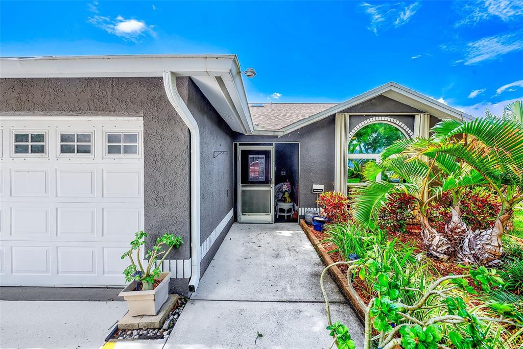 A gray house exterior features a white garage door, a front entryway, and tropical landscaping — 7969 SOMERSET DRIVE, LARGO, FL