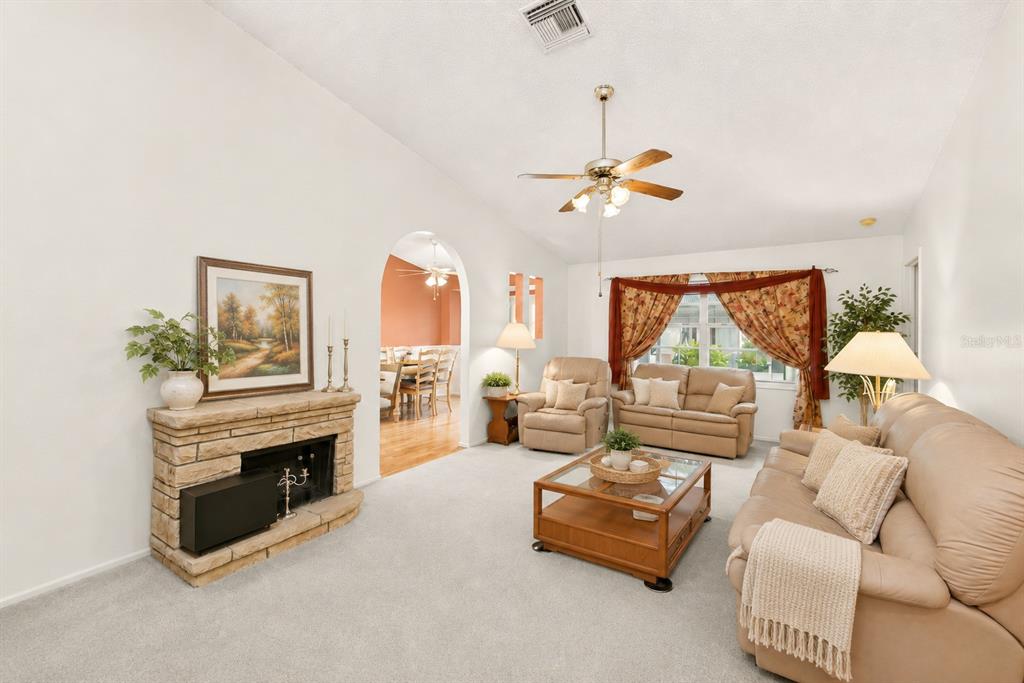 A living room features a stone fireplace, beige furniture, and an arched doorway to a dining area — 7969 SOMERSET DRIVE, LARGO, FL