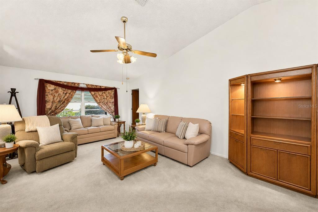 A living room features beige carpet, two sofas, an armchair, and a large wooden cabinet — 7969 SOMERSET DRIVE, LARGO, FL
