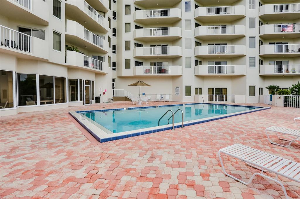 A rectangular swimming pool sits on a paved patio surrounded by a multi-story apartment building — 3 OCEANS WEST BOULEVARD UNIT 7C1, DAYTONA BEACH, FL