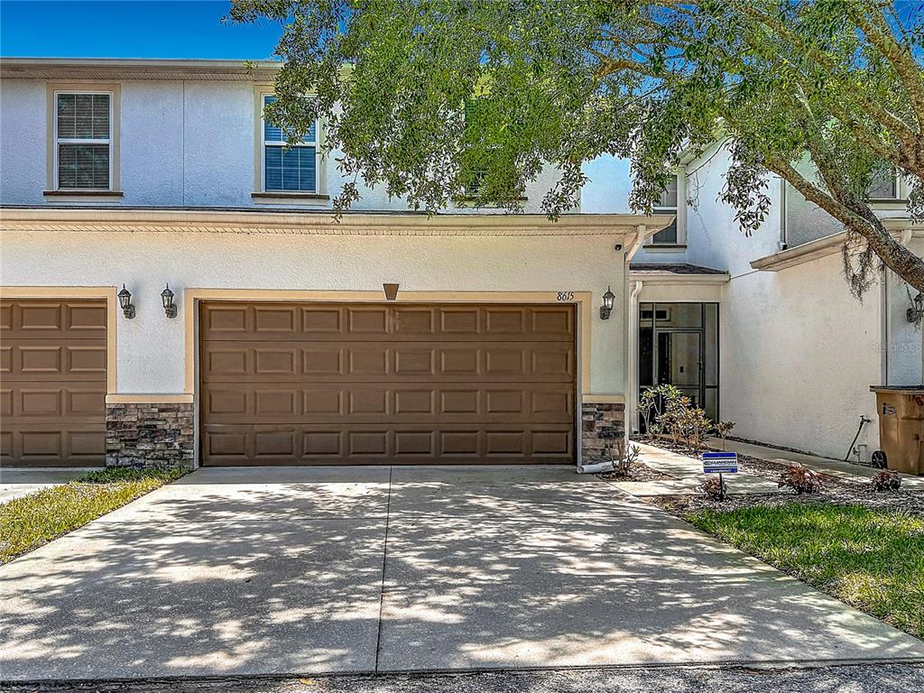 A two-story townhouse exterior features a brown garage door, a concrete driveway, and stone accents — 8615 ANDALUCIA FIELD DRIVE, TAMPA, FL