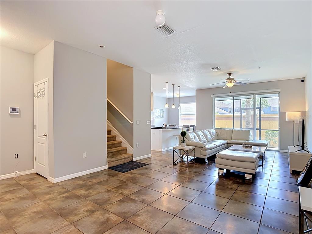 A living room with tile floors, a white sectional sofa, and stairs leading upstairs — 8615 ANDALUCIA FIELD DRIVE, TAMPA, FL