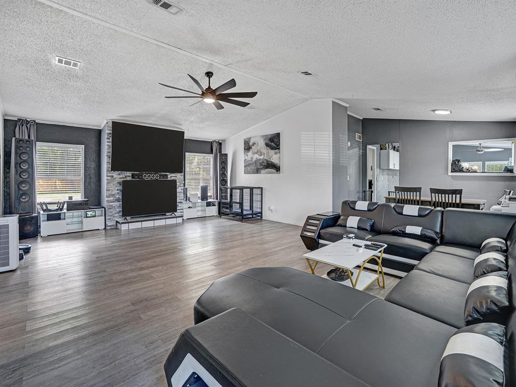 A living room features a large sectional sofa, a stone fireplace with dual televisions, and wood-look flooring — 12845 CASA BIANCA AVENUE, NEW PORT RICHEY, FL